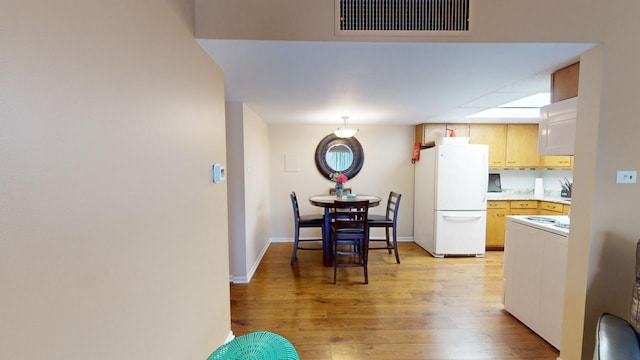 kitchen with light brown cabinetry, light hardwood / wood-style flooring, and white fridge