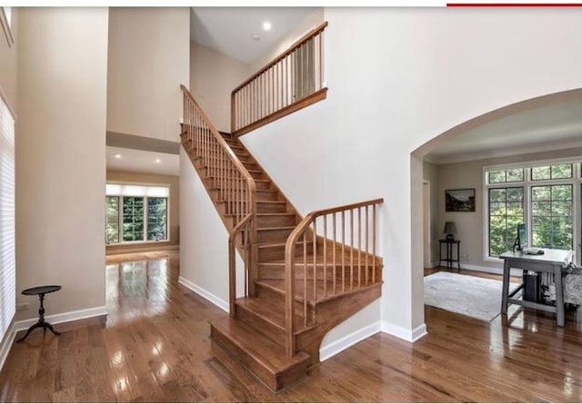 stairway with hardwood / wood-style floors and a towering ceiling