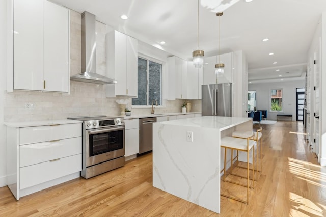 kitchen featuring pendant lighting, stainless steel appliances, white cabinetry, and wall chimney range hood