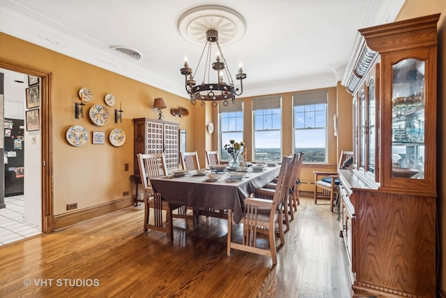 dining space with light hardwood / wood-style floors, crown molding, and an inviting chandelier