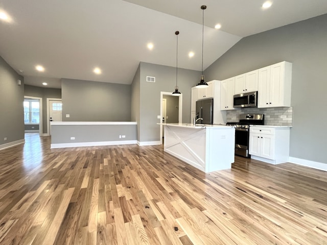 kitchen with appliances with stainless steel finishes, tasteful backsplash, a center island with sink, white cabinetry, and hanging light fixtures