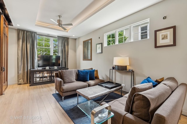 living room featuring ceiling fan, light hardwood / wood-style floors, and a tray ceiling