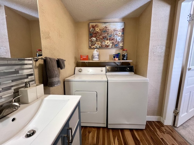 clothes washing area with sink, washing machine and dryer, a textured ceiling, and dark wood-type flooring