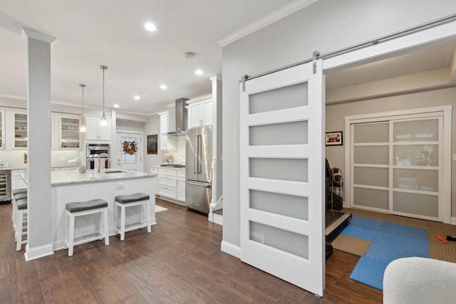 kitchen featuring white cabinets, appliances with stainless steel finishes, a kitchen breakfast bar, and wall chimney range hood