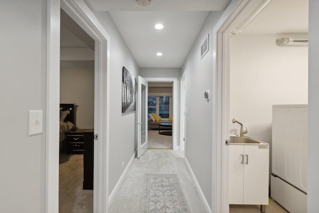 hallway with light carpet, sink, and washer / dryer