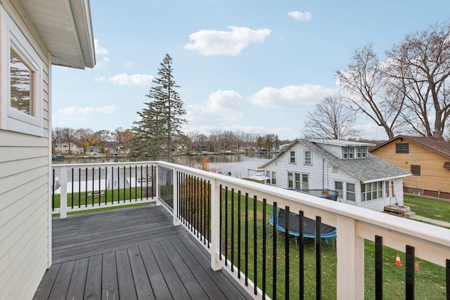 wooden terrace with a trampoline, a water view, and a lawn