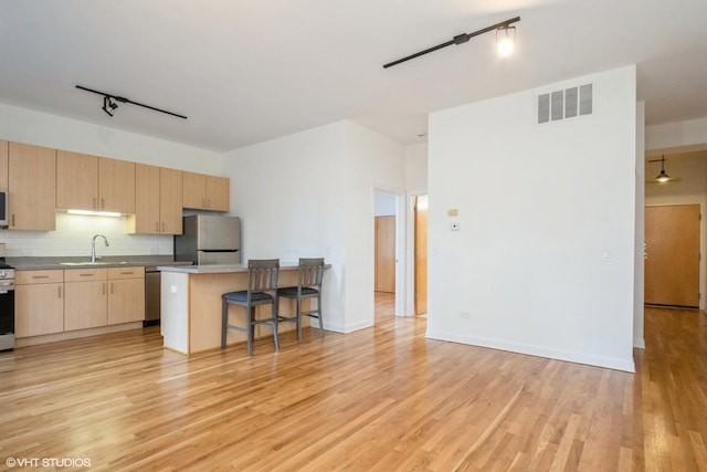 kitchen featuring a center island, light hardwood / wood-style flooring, appliances with stainless steel finishes, tasteful backsplash, and a breakfast bar area