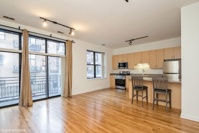 kitchen featuring sink, a breakfast bar area, light wood-type flooring, light brown cabinetry, and stainless steel appliances