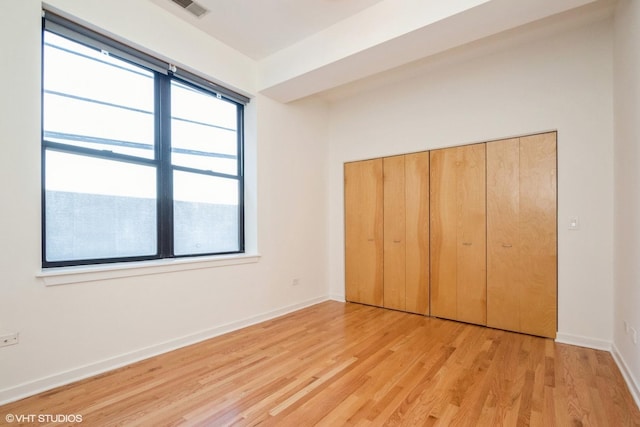 unfurnished bedroom featuring multiple windows, light hardwood / wood-style flooring, and a closet