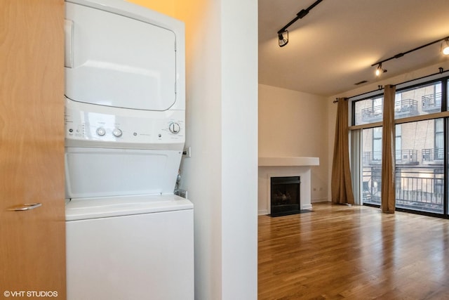 clothes washing area featuring wood-type flooring, rail lighting, and stacked washer and dryer