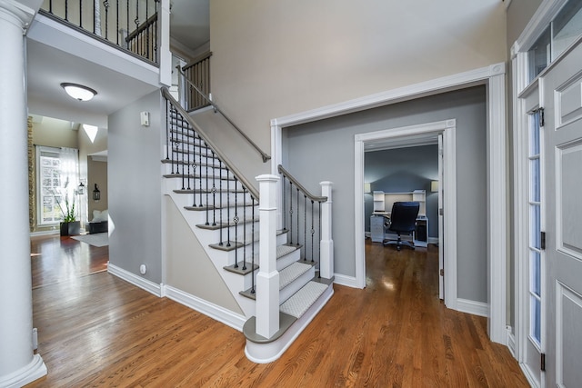 entrance foyer with decorative columns, a towering ceiling, and dark wood-type flooring