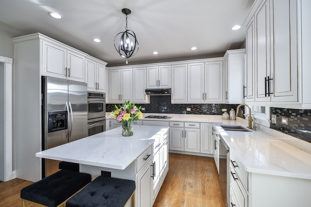 kitchen with stainless steel appliances, sink, decorative light fixtures, a center island, and white cabinetry