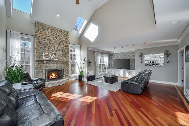 living room with a skylight, rail lighting, hardwood / wood-style floors, a fireplace, and ornamental molding