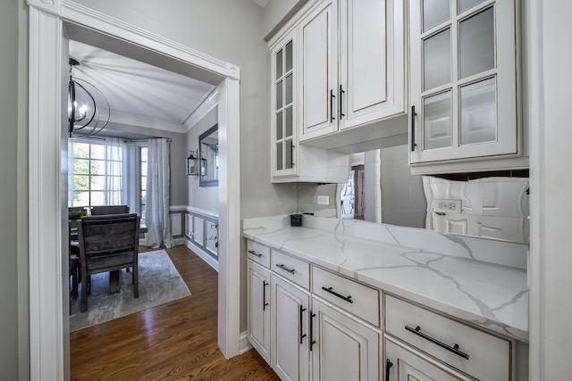 kitchen with white cabinetry, light stone countertops, dark hardwood / wood-style floors, a chandelier, and ornamental molding