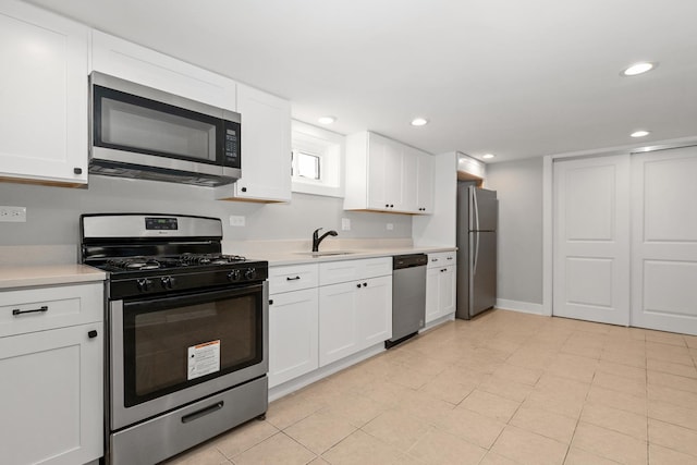 kitchen with appliances with stainless steel finishes, sink, white cabinetry, and light tile patterned flooring