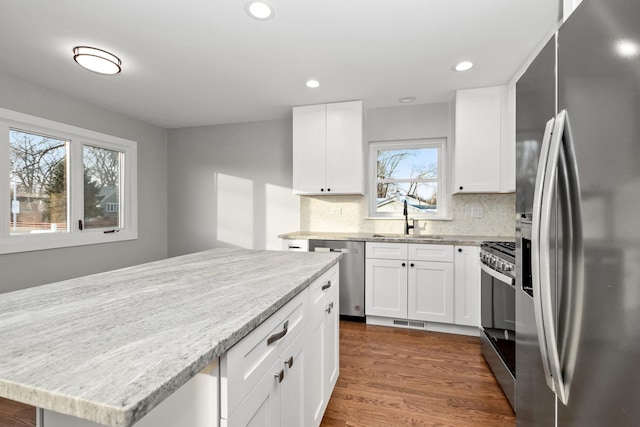 kitchen featuring tasteful backsplash, sink, white cabinetry, appliances with stainless steel finishes, and light stone counters