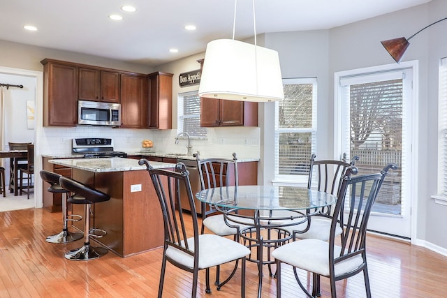 kitchen featuring stainless steel appliances, sink, decorative light fixtures, light hardwood / wood-style floors, and a kitchen island