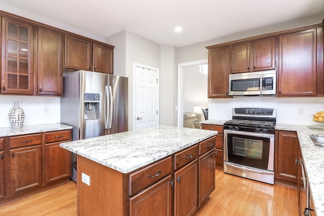 kitchen featuring light hardwood / wood-style flooring, tasteful backsplash, a kitchen island, light stone counters, and stainless steel appliances