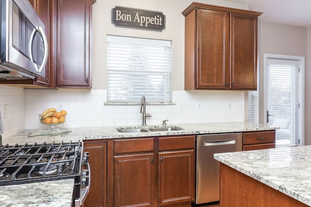 kitchen with appliances with stainless steel finishes, tasteful backsplash, light stone counters, and sink