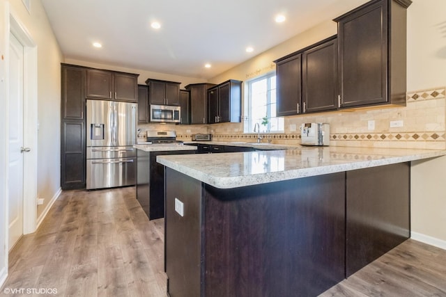 kitchen with light stone countertops, kitchen peninsula, appliances with stainless steel finishes, and light hardwood / wood-style flooring