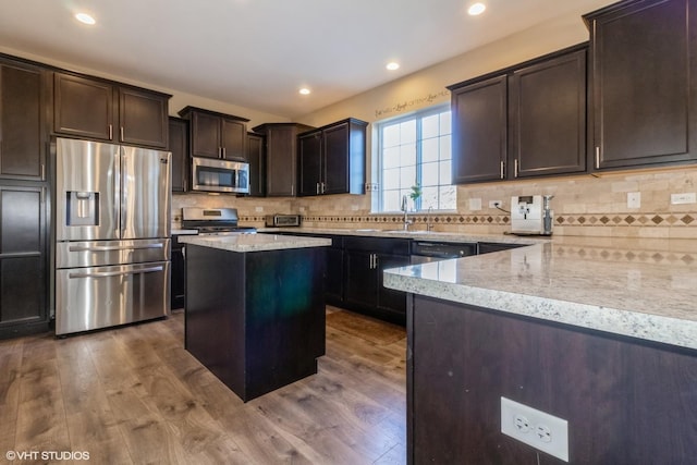 kitchen with light stone countertops, appliances with stainless steel finishes, hardwood / wood-style flooring, and a kitchen island