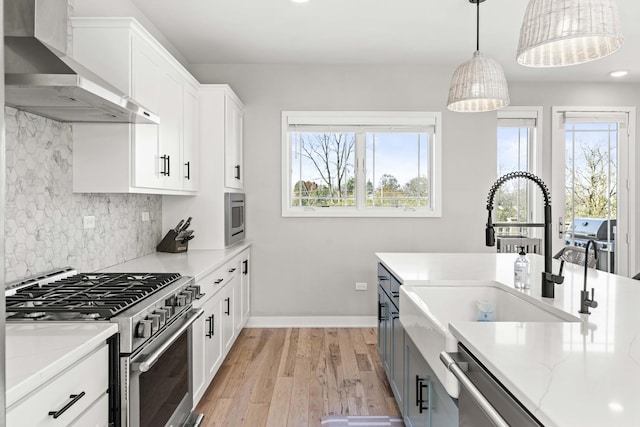 kitchen with white cabinets, high end stainless steel range, wall chimney exhaust hood, light stone countertops, and decorative light fixtures