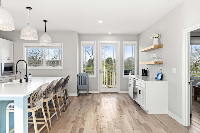 kitchen featuring stainless steel microwave, hanging light fixtures, light hardwood / wood-style floors, a kitchen bar, and white cabinetry