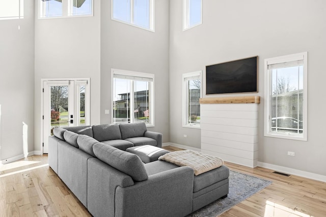 living room featuring a towering ceiling, light hardwood / wood-style floors, and a healthy amount of sunlight