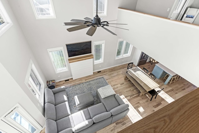 living room featuring a towering ceiling, light hardwood / wood-style flooring, ceiling fan, and plenty of natural light