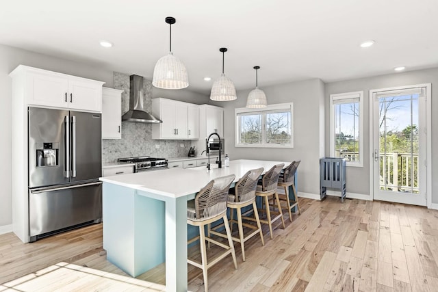 kitchen with wall chimney exhaust hood, premium appliances, pendant lighting, white cabinets, and an island with sink