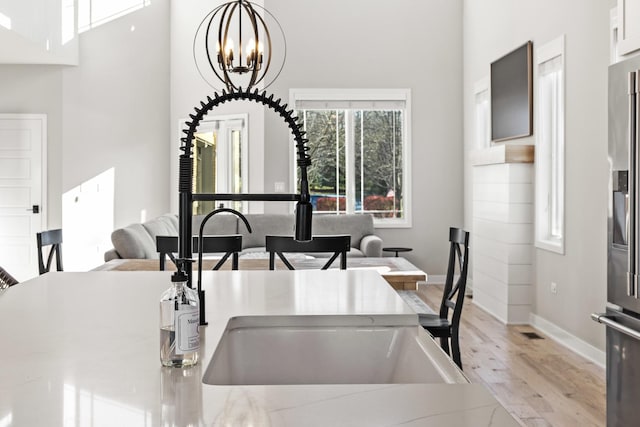 kitchen with pendant lighting, sink, light hardwood / wood-style flooring, a notable chandelier, and stainless steel fridge with ice dispenser