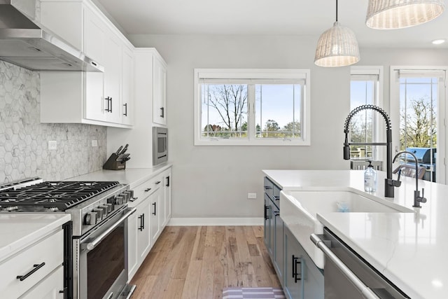 kitchen with wall chimney range hood, tasteful backsplash, decorative light fixtures, white cabinets, and appliances with stainless steel finishes