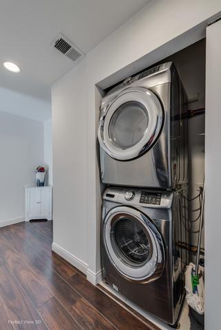 laundry room featuring stacked washer / drying machine and dark wood-type flooring