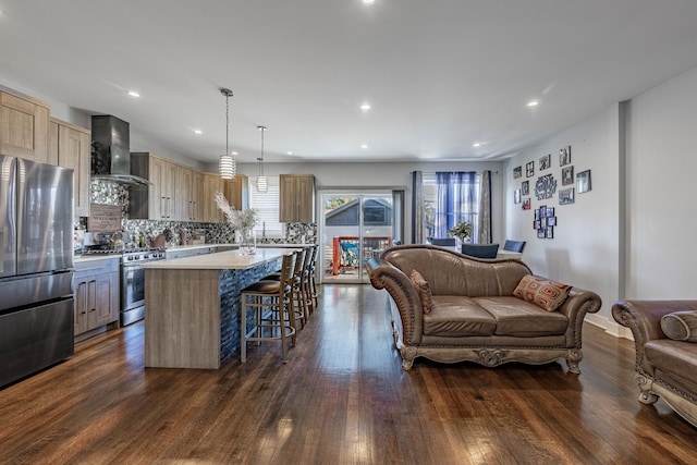 kitchen with a kitchen island, pendant lighting, dark hardwood / wood-style flooring, stainless steel appliances, and wall chimney range hood