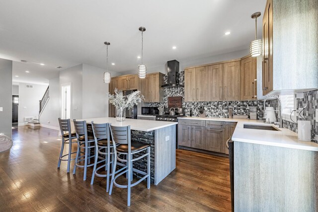 kitchen featuring sink, a breakfast bar area, a center island, pendant lighting, and wall chimney range hood