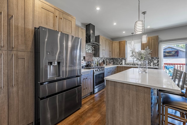 kitchen with a kitchen island, appliances with stainless steel finishes, pendant lighting, a kitchen breakfast bar, and wall chimney range hood