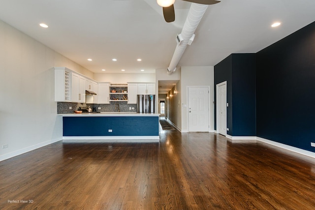 kitchen with kitchen peninsula, dark hardwood / wood-style floors, decorative backsplash, white cabinetry, and stainless steel refrigerator