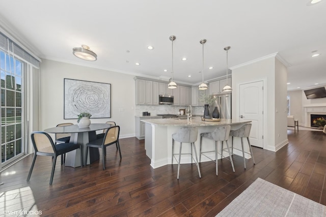 kitchen with backsplash, gray cabinetry, stainless steel appliances, a center island with sink, and hanging light fixtures