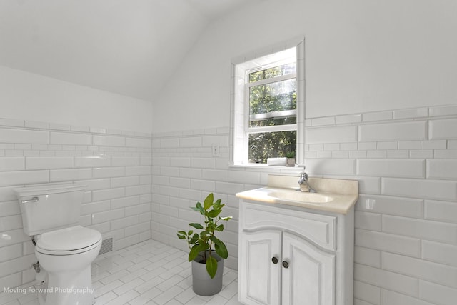 bathroom featuring vanity, vaulted ceiling, tile patterned flooring, toilet, and tile walls