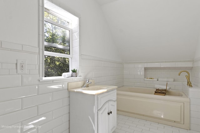 bathroom featuring tile patterned flooring, a bath, vaulted ceiling, vanity, and tile walls