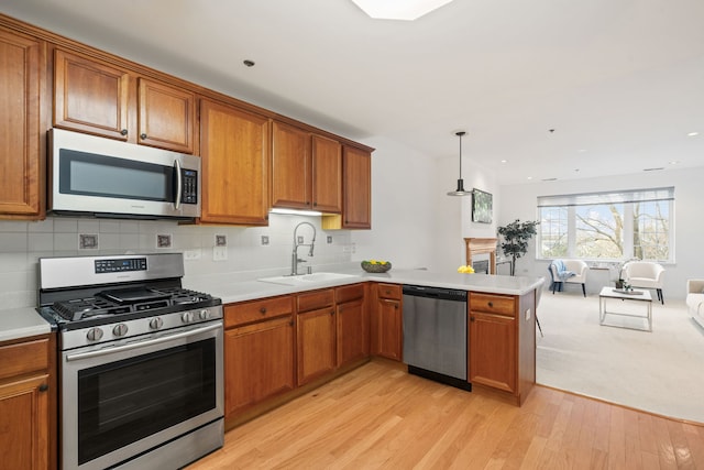 kitchen with kitchen peninsula, stainless steel appliances, sink, decorative light fixtures, and light hardwood / wood-style floors