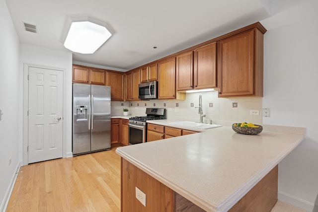 kitchen with backsplash, sink, light hardwood / wood-style floors, kitchen peninsula, and stainless steel appliances