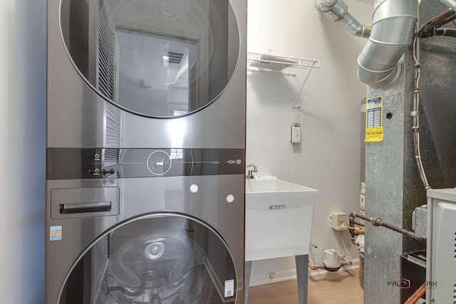 laundry room featuring heating unit, stacked washer / dryer, hardwood / wood-style flooring, and sink