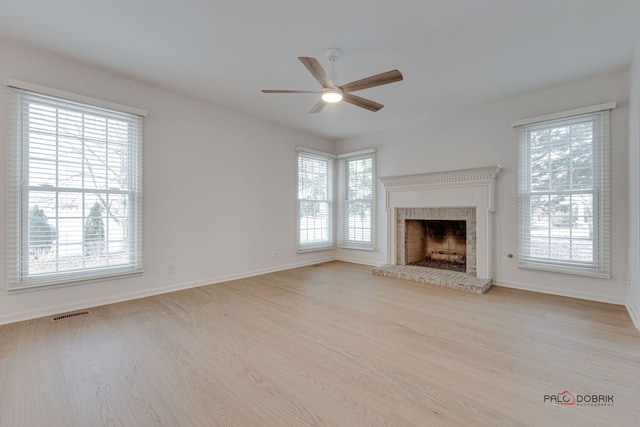 unfurnished living room featuring plenty of natural light, light wood-type flooring, and a brick fireplace