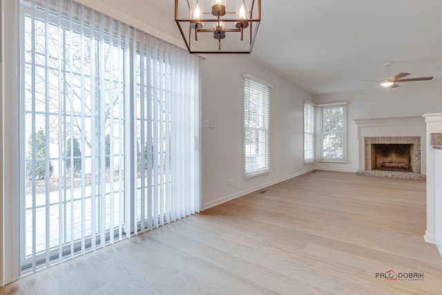 unfurnished living room featuring ceiling fan with notable chandelier, light hardwood / wood-style floors, and a fireplace