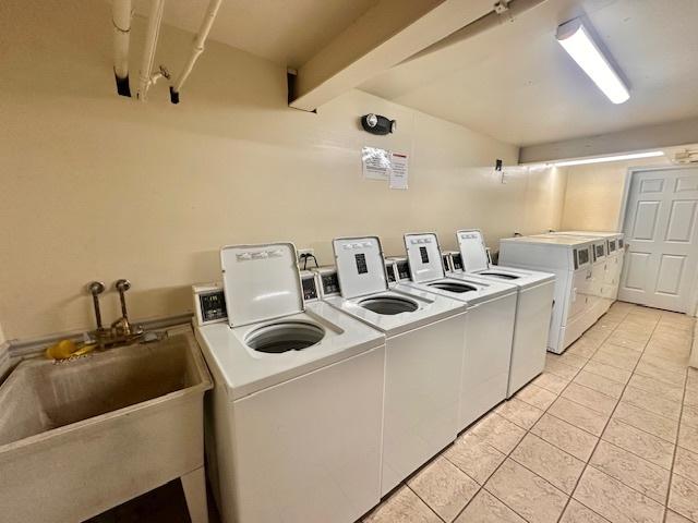 clothes washing area featuring washer and clothes dryer, light tile patterned floors, and sink