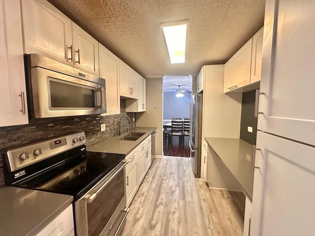 kitchen with appliances with stainless steel finishes, ceiling fan, sink, white cabinets, and light hardwood / wood-style floors