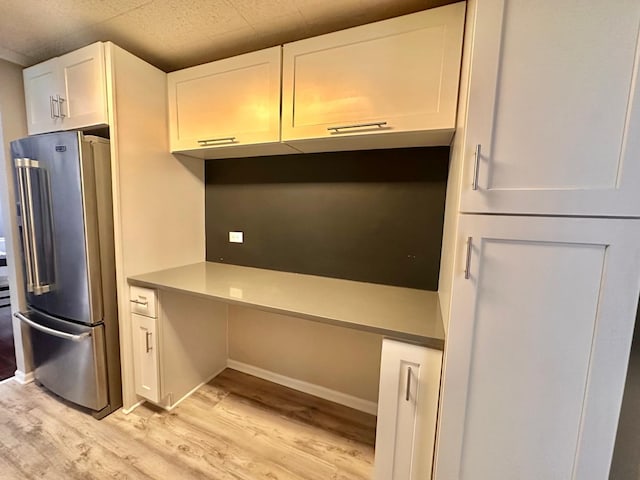 kitchen with high end refrigerator, light hardwood / wood-style flooring, white cabinets, and built in desk