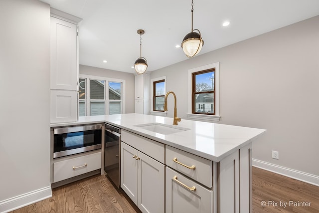 kitchen featuring sink, dishwasher, white cabinetry, stainless steel microwave, and decorative light fixtures