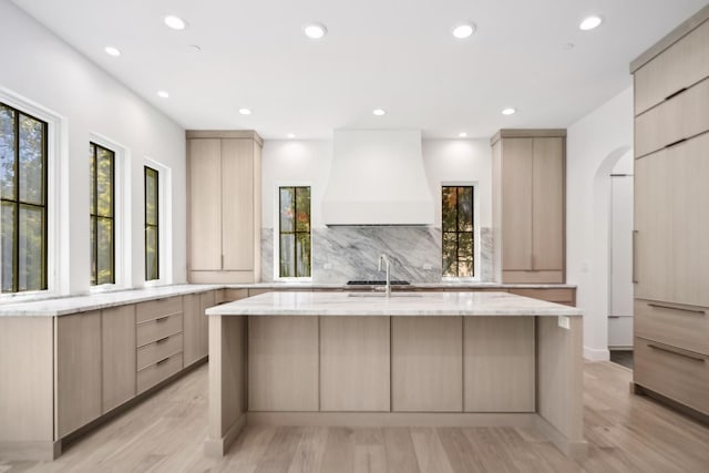 kitchen featuring a kitchen island with sink, light brown cabinetry, light wood-type flooring, and custom exhaust hood